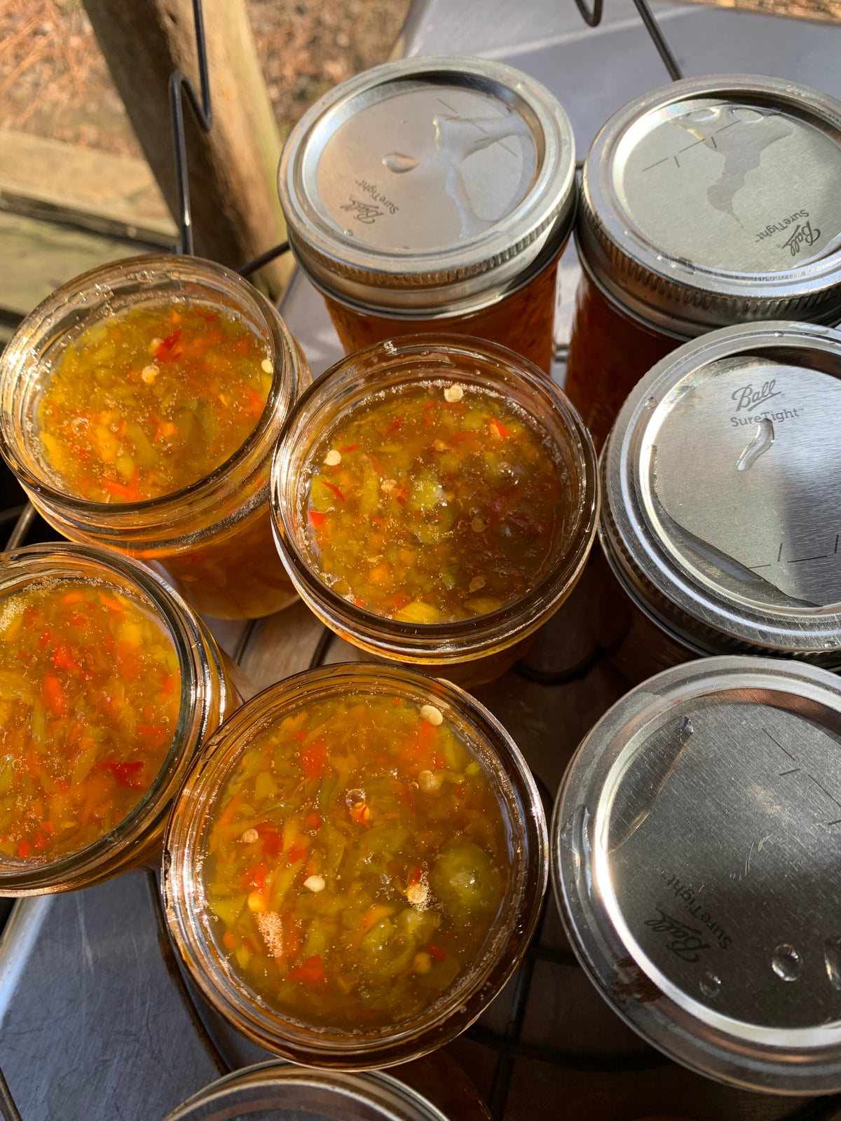 Several jars filled with hot pepper jelly in the metal rack of a hot water bath canner. 